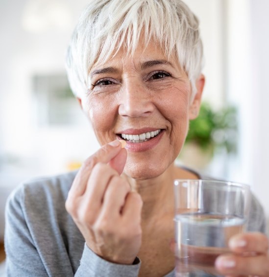 Senior woman holding pill and glass of water