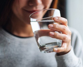 Nose-to-chest view of someone in grey sweater sipping water