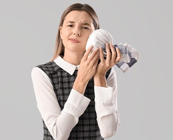 Woman in checkered dress applying cold compress to sore face