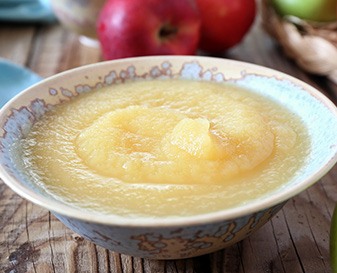 Ceramic bowl of applesauce on wooden table with red and green apples