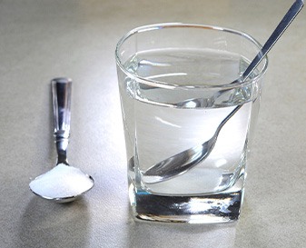 Spoon of salt next to glass of water with spoon in it