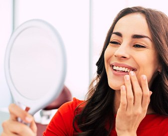 Woman in red-orange shirt admiring her smile in circular handheld mirror